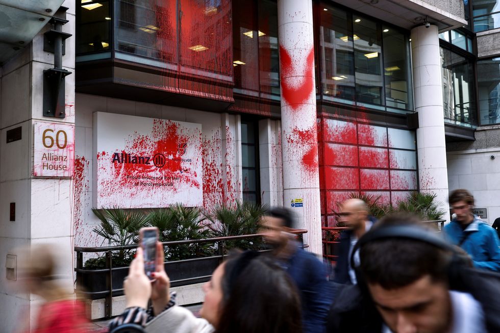 People walk near an office building occupied by a unit of Allianz, which was covered in red paint in London,