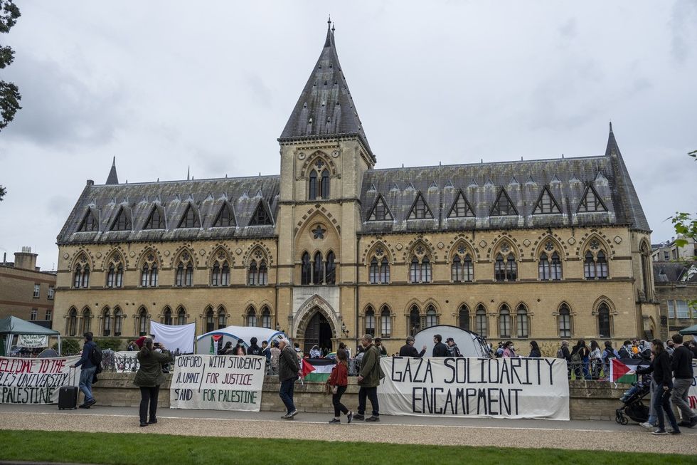 People walk past a pro-Palestine encampment set up by student activists in front of the Oxford University Museum of Natural History