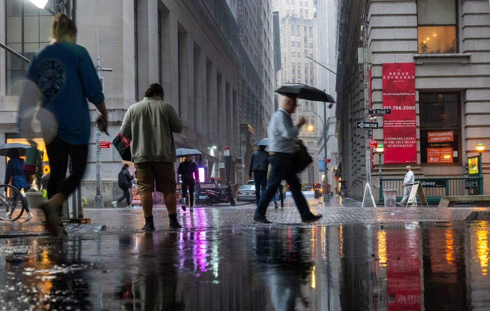 People walk through the morning rain by the New York Stock Exchange (NYSE)
