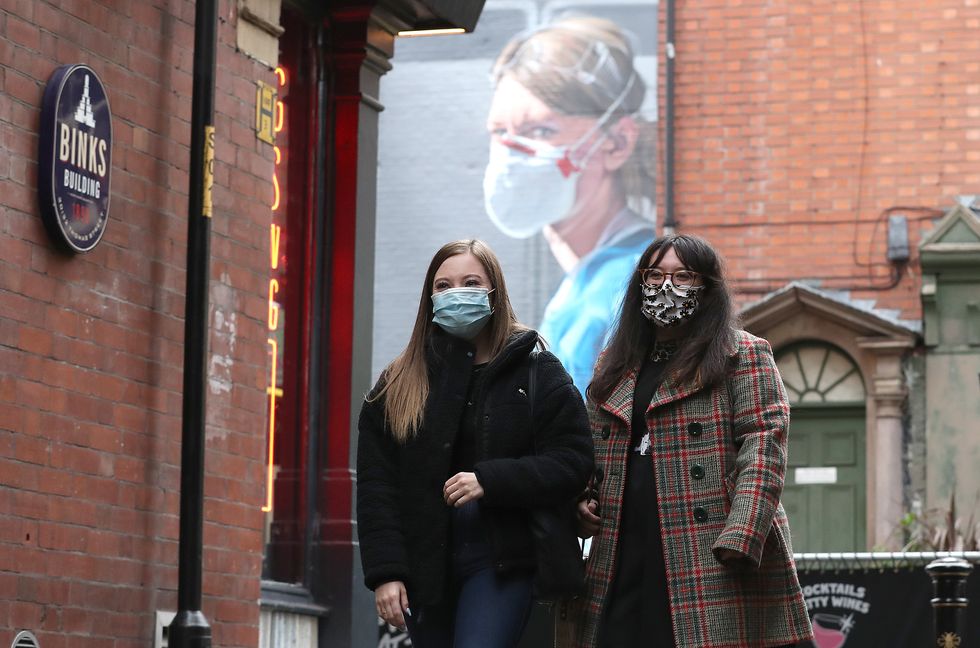 People wearing a face mask walk near a mural of a nurse in the Northern Quarter of Manchester.