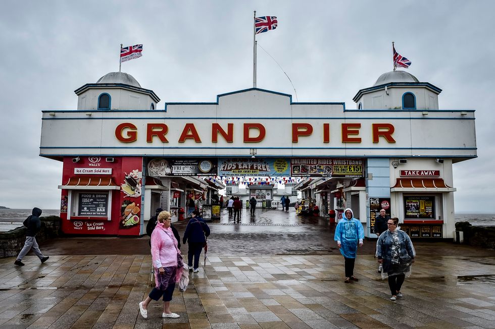 People wearing ponchos walk from the Grand Pier at Weston-super-Mare in Somerset as rain and wind batter Britain's western coastline.
