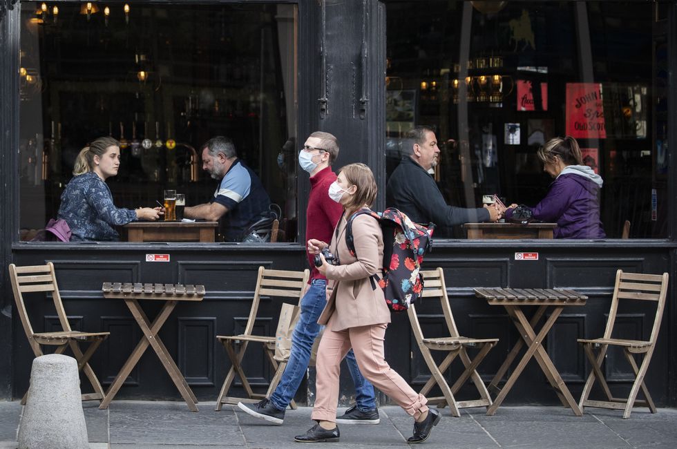 People wearing protective face masks walk past a bar in Edinburgh.
