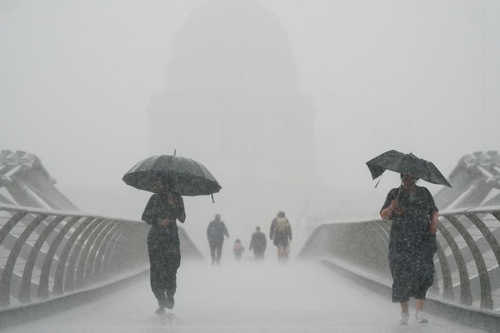 People with umbrellas walking in the rain on Millennium Bridge, London