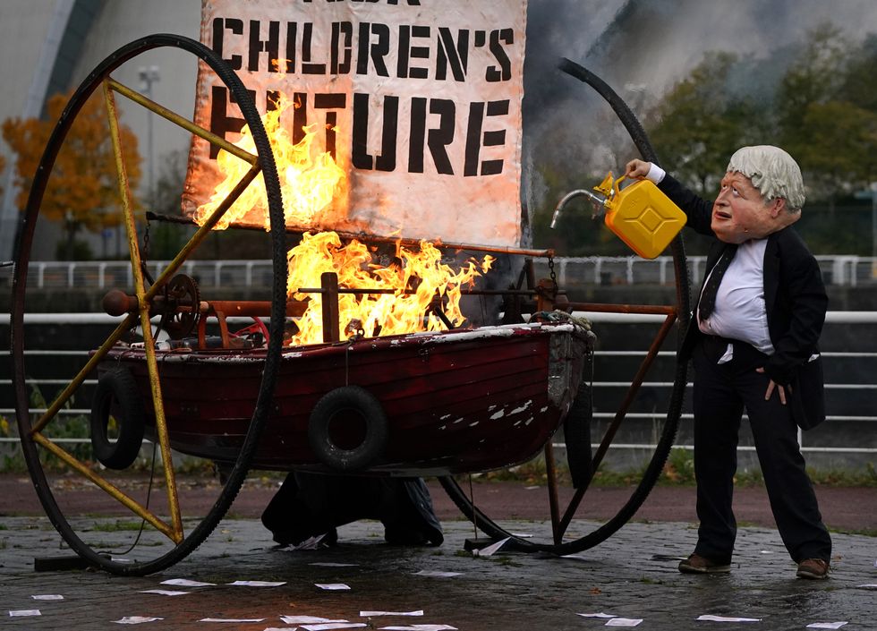 Performers from Ocean Rebellion dressed as Prime Minister Boris Johnson and an Oilhead set light to the sail of a small boat which reads \%22Your Children's Future\%22 as they burn stacks of money on the banks of the River Clyde in Glasgowm close to the site of the upcoming Cop26 conference.