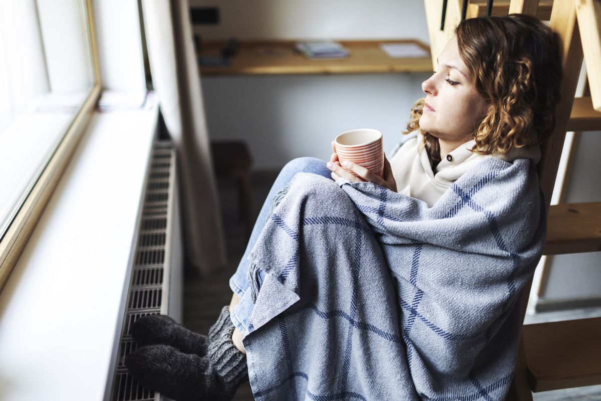 Person cold sits in blanket and socks by radiator