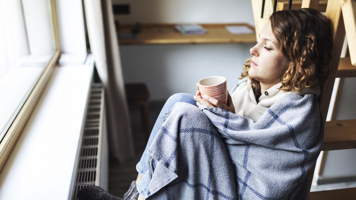 Person cold sits in blanket and socks by radiator