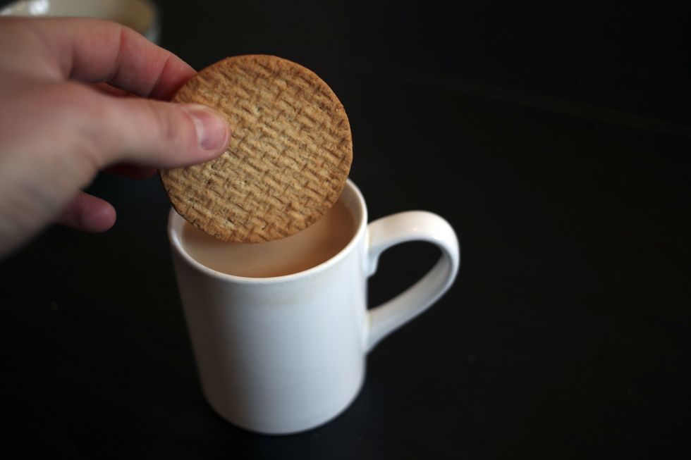 Person dipping biscuit in cup of tea