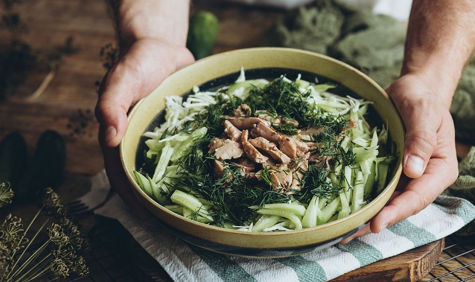 Person holding bowl of leafy greens and cod liver