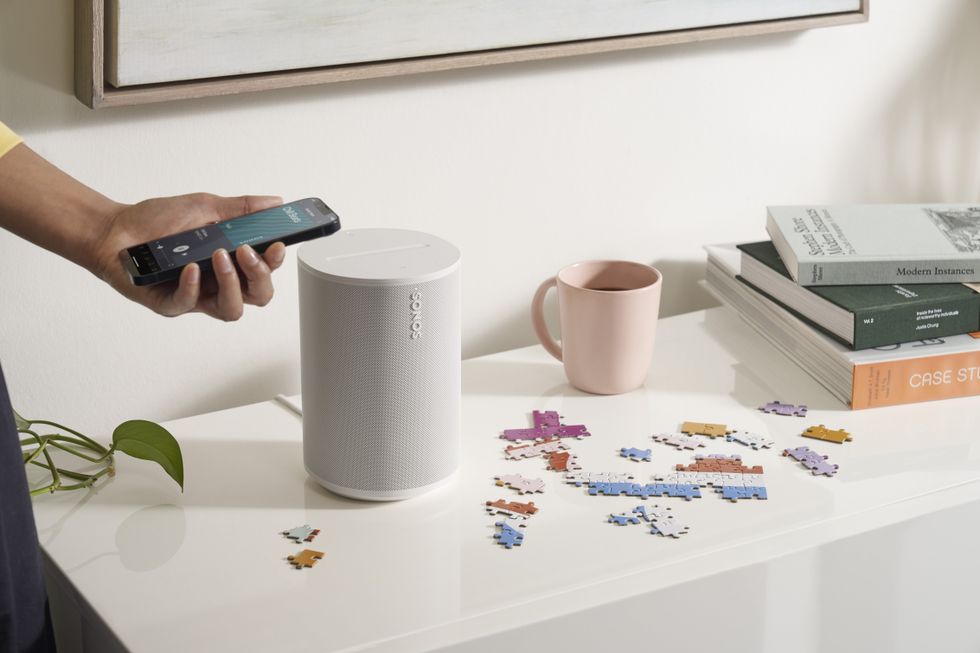 person holds a smartphone above a sonos era 100 speaker