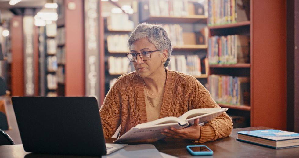 Person looks at book and laptop