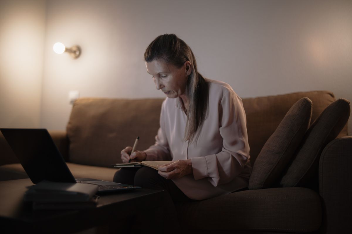 Person looks at finances on sofa with laptop in front of her
