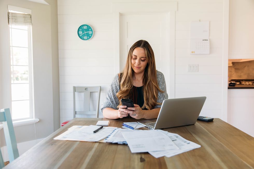 Person looks at phone beside laptop