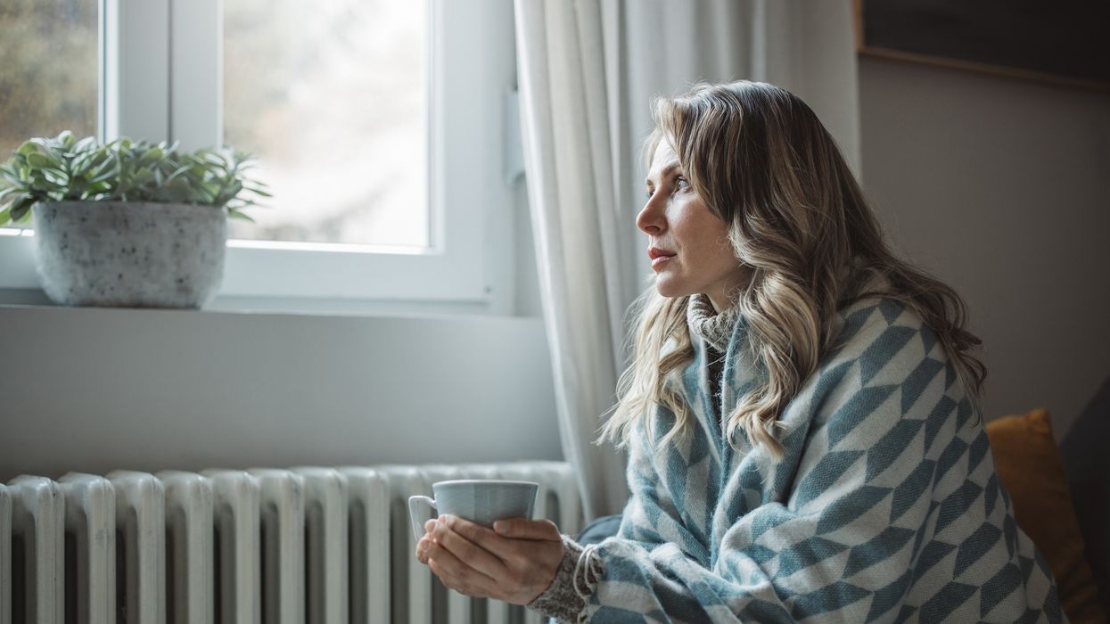 Person looks cold in blanket by radiator with mug in hands