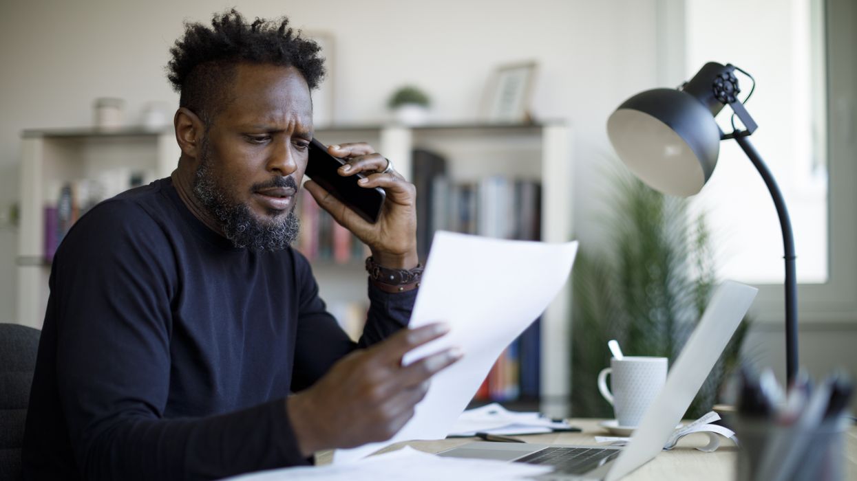 Person looks worried at letter while on phone and beside laptop