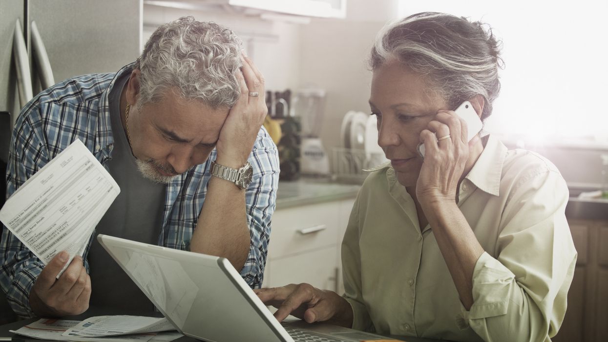 Person on phone looking at laptop while partner looks at documents
