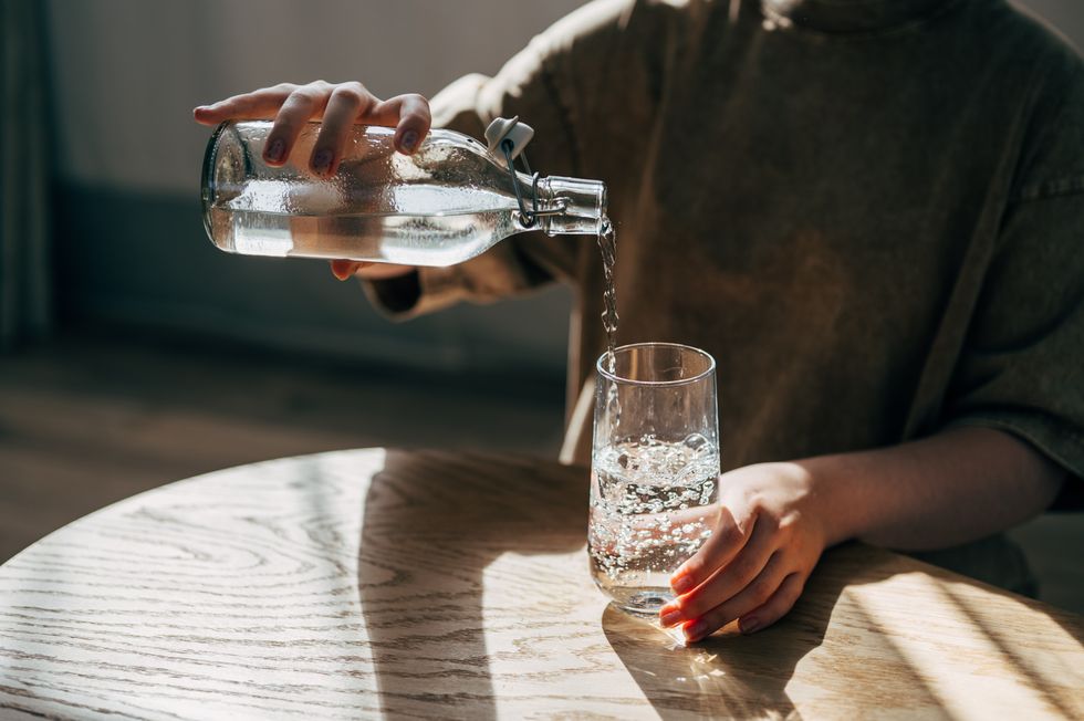 Person pouring water from a glass bottle into a glass