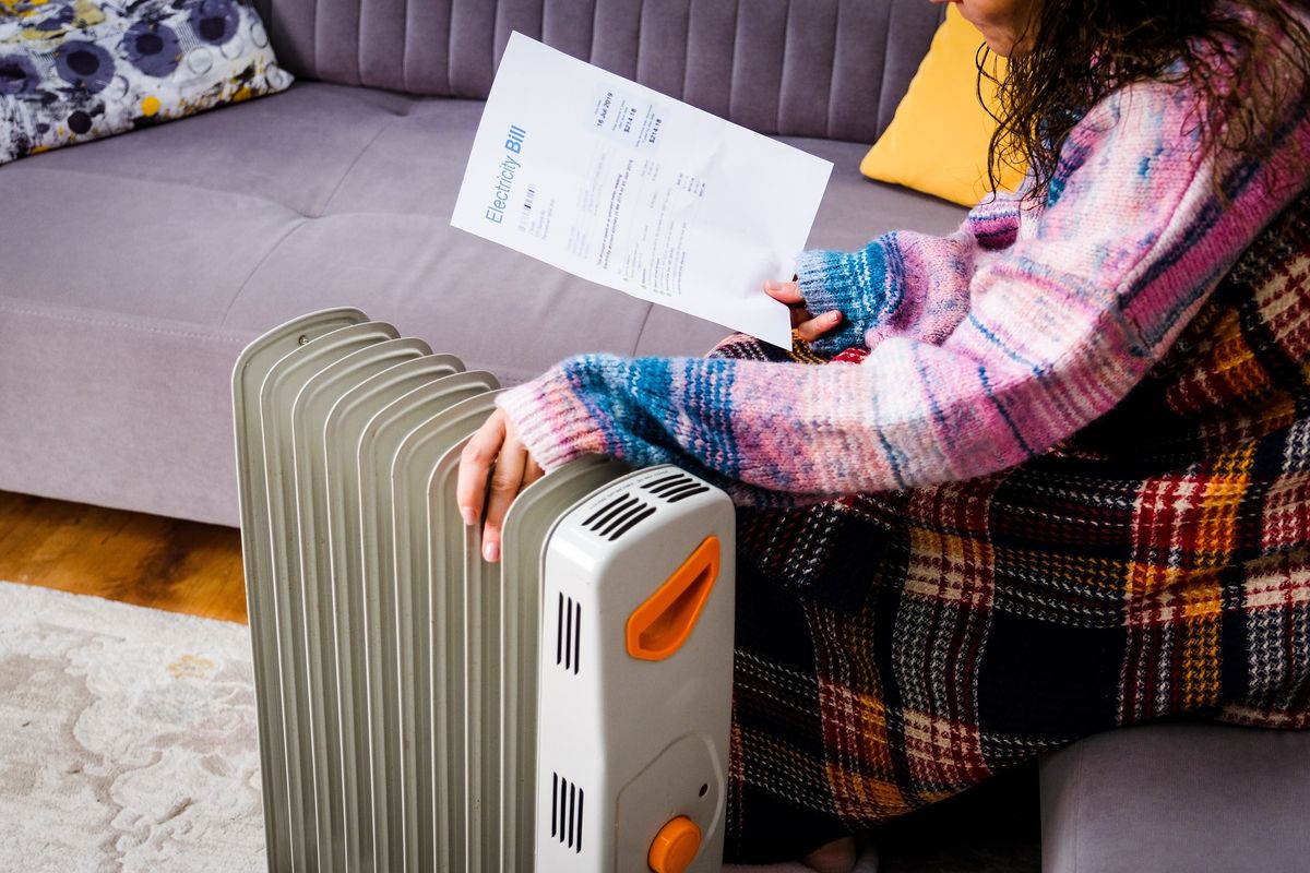 Person sits by heater with electricity bill during very cold weather in pictures