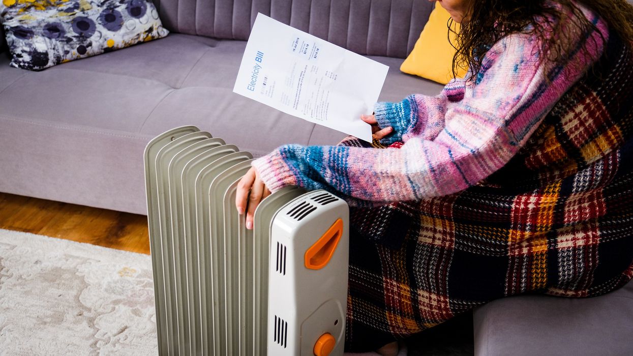 Person sits by heater with electricity bill during very cold weather in pictures