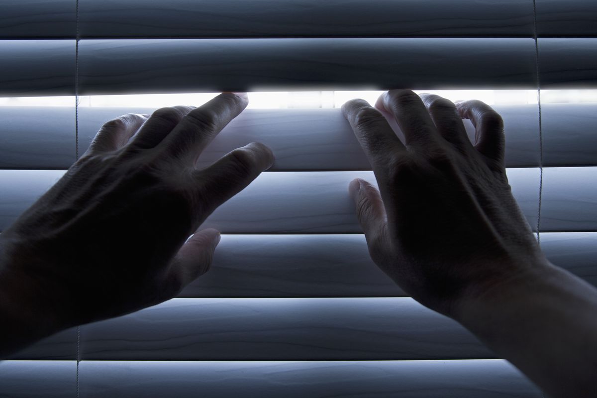 Person using their hands to peer through their blinds 