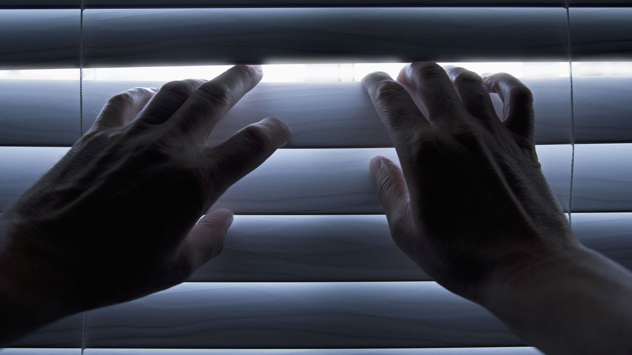 Person using their hands to peer through their blinds