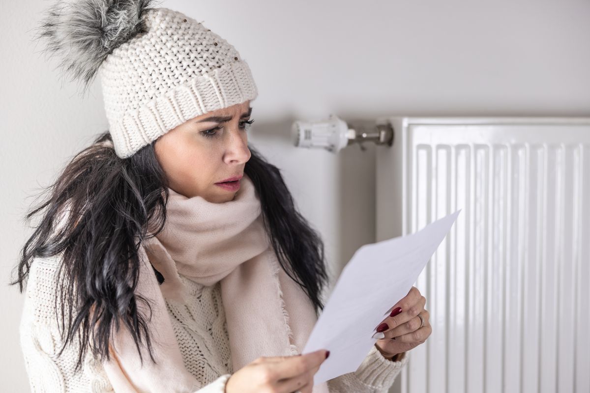 Person wears warm hat and looks at energy bill statement during very cold weather
