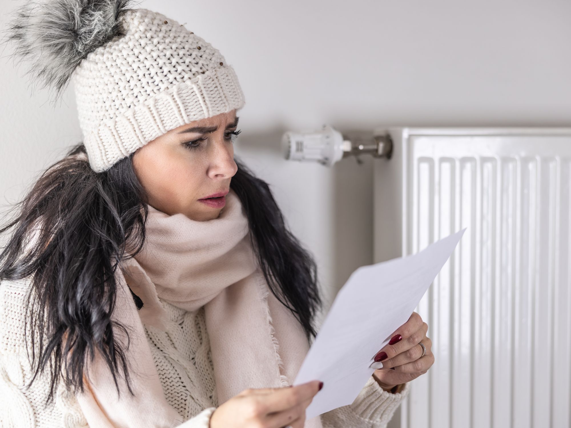 Person wears warm hat and looks at energy bill statement during very cold weather