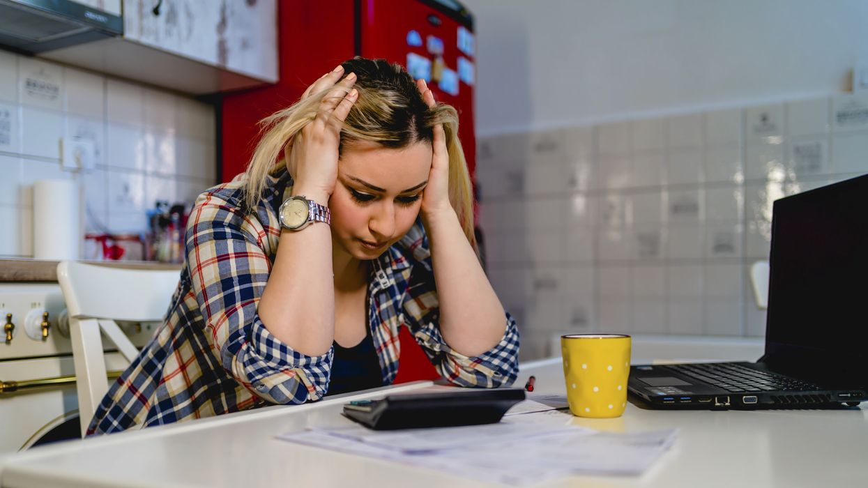 Person with head in hands as they look at calculator, laptop and documents