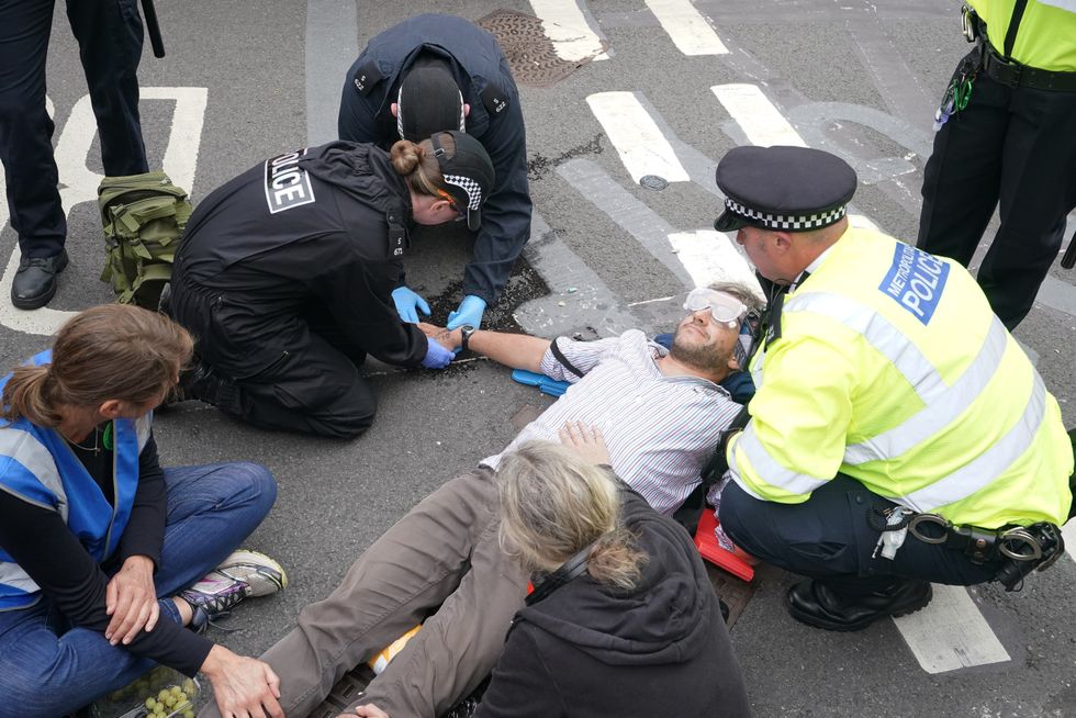 Police attempt to free a man who has glued himself to the road during a protest by members of Extinction Rebellion on London Bridge, in central London. Picture date: Tuesday August 31, 2021.