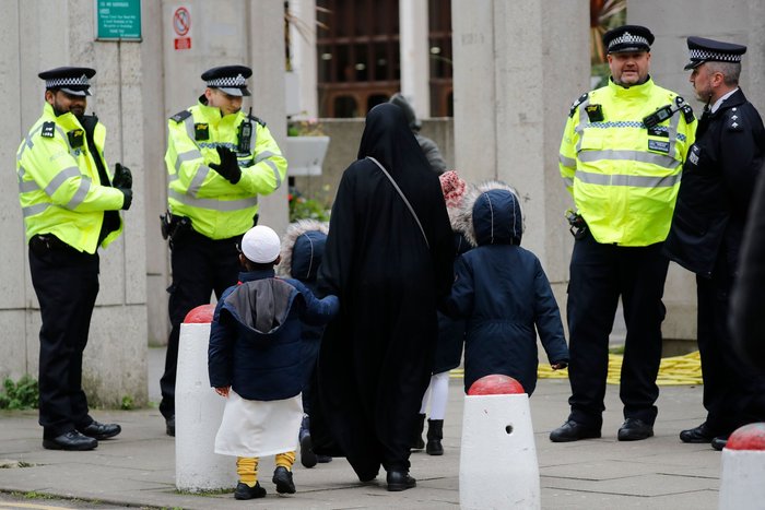 Police in London watch as a Muslim woman and her children walk past