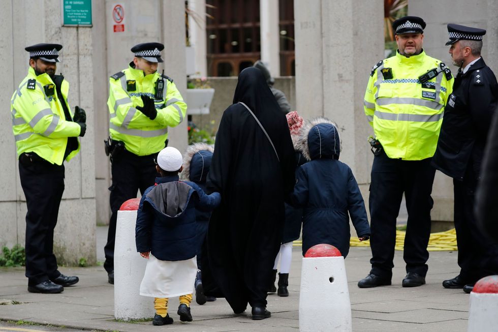 Police in London watch as a Muslim woman and her children walk past