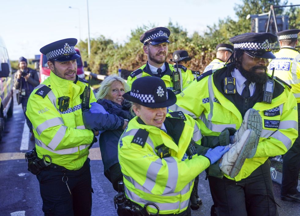 Police officers detain a protester from Insulate Britain occupying a roundabout leading from the M25 motorway to Heathrow Airport in London.