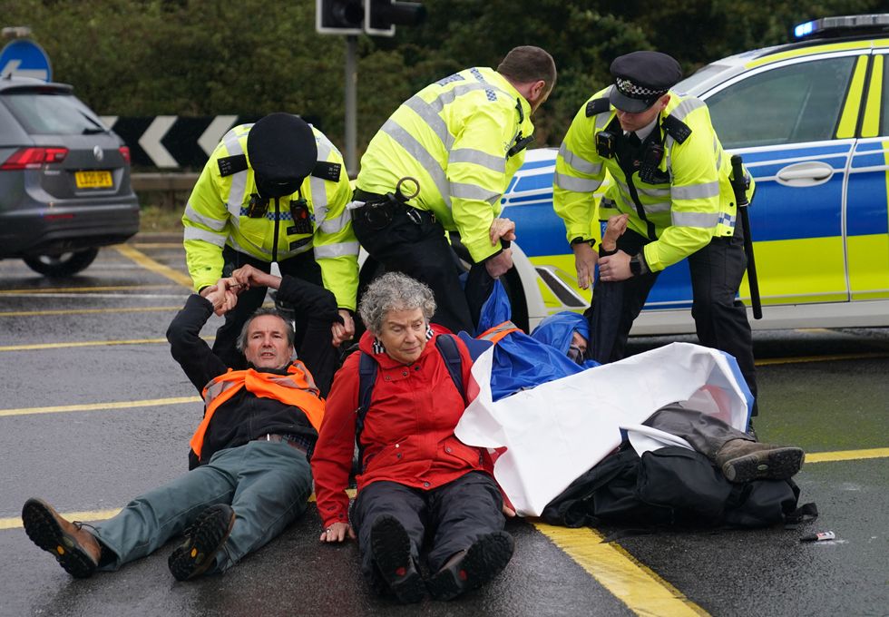 Police officers detain protesters from Insulate Britain occupying a roundabout leading from the M25 motorway to Heathrow Airport in London. Picture date: Monday September 27, 2021.