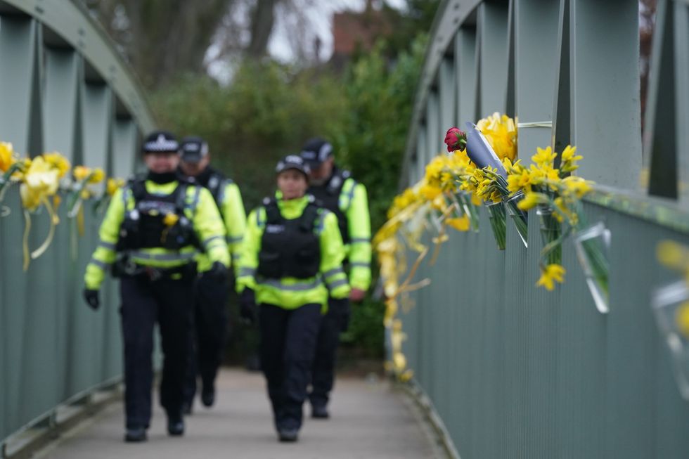 Police officers walk past flowers and yellow ribbons tied to a bridge for Nicola Bulley over the River Wyre in St Michael's on Wyre, Lancashire, where police recovered a body on Sunday, which was found by members of the public close to where Nicola Bulley disappeared on January 27. Ms Bulley, 45, was last seen walking her dog nearby, on a footpath along the River Wyre, after dropping her daughters, aged six and nine, at school. Picture date: Monday February 20, 2023.