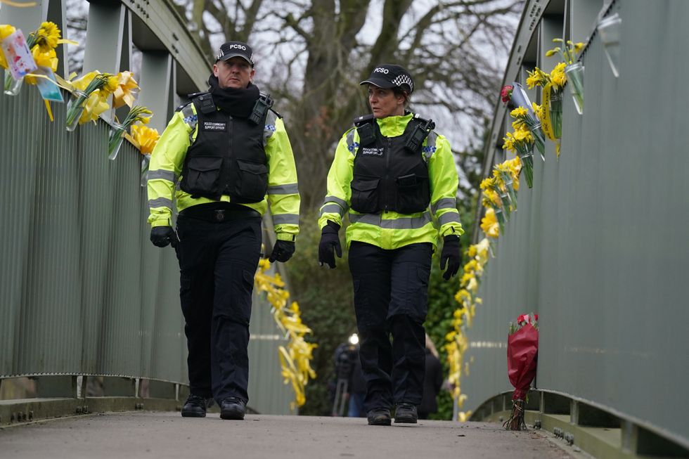 Police officers walk past flowers and yellow ribbons tied to a bridge over the River Wyre