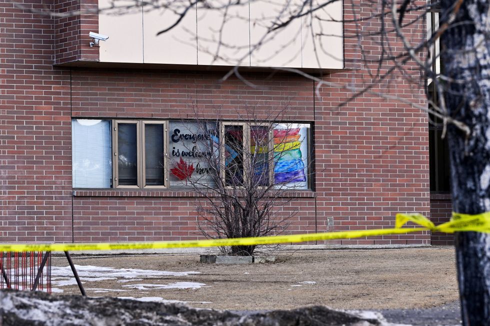 Police tape blows in the wind in front of a window at Tumbler Ridge Secondary School bearing the message 'everyone is welcome here' alongside a Canadian maple leaf and a 'progress' Pride flag\u200b