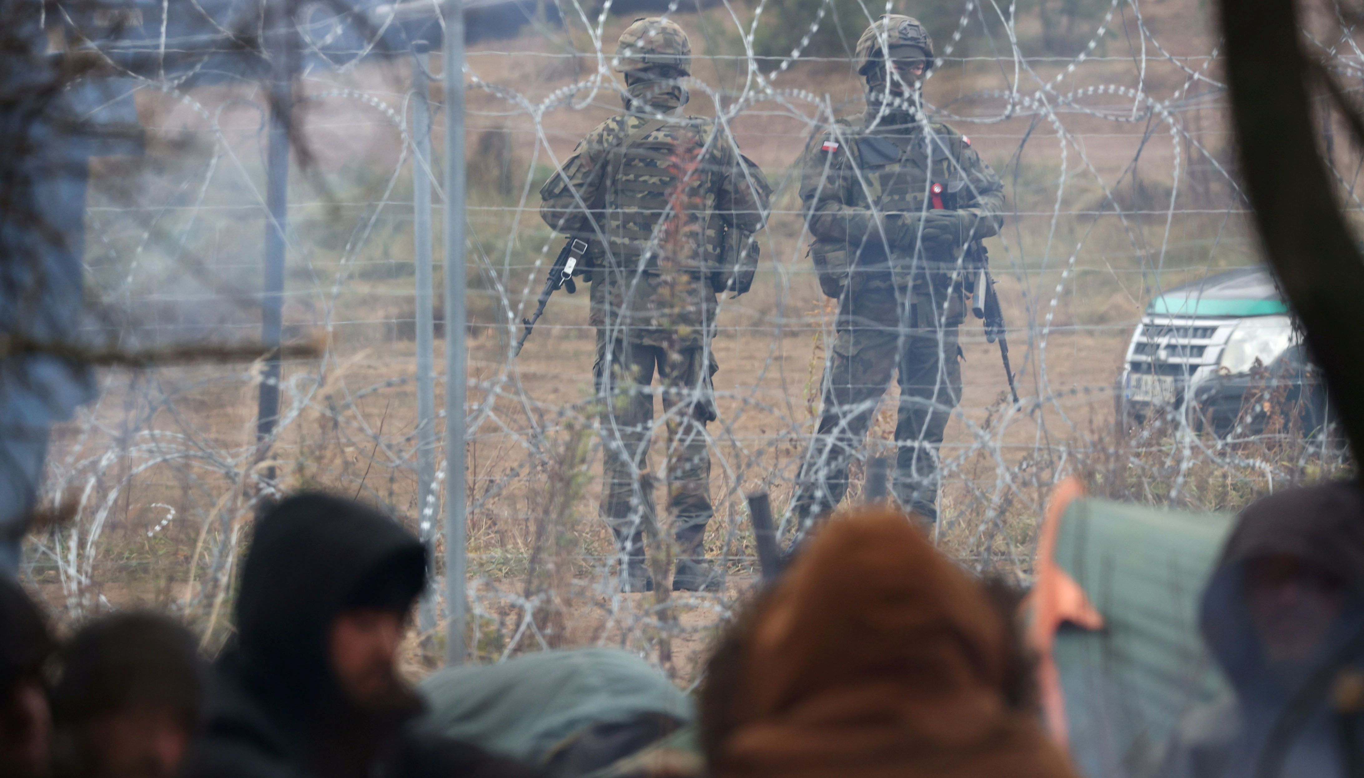 Polish service members are seen through a barbed wire fence as hundreds of migrants gather on the Belarusian-Polish border in an attempt to cross it in the Grodno region, Belarus November 10, 2021.