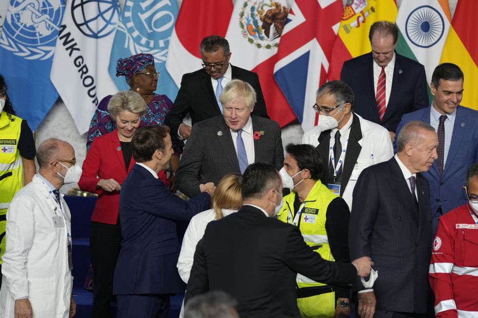 Prime Minister Boris Johnson (center) and French President Emmanuel Macron do a fist bump as they gather with other world leaders gather for a group picture at the La Nuvola conference center during the G20 summit.