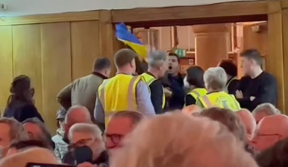 Protester is ejected from the meeting heckling Jeremy Corbyn and wielding a Ukraine flag.