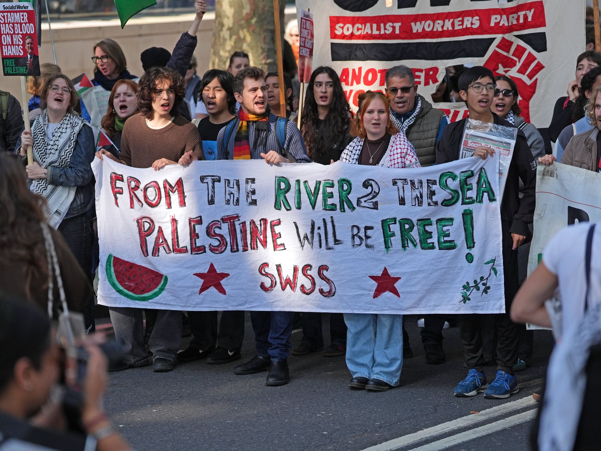 Protesters marching holding a sign reading: 'From the river to the sea, Palestine will be free'