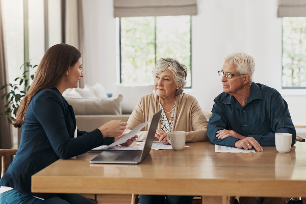 Real estate agent speaking with older couple at a table in front of papers and an open laptop