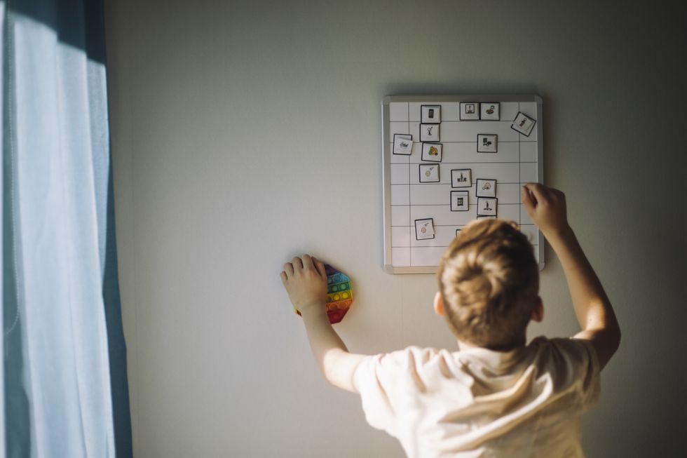 Rear view of boy going through weekly planner mounted on wall at home