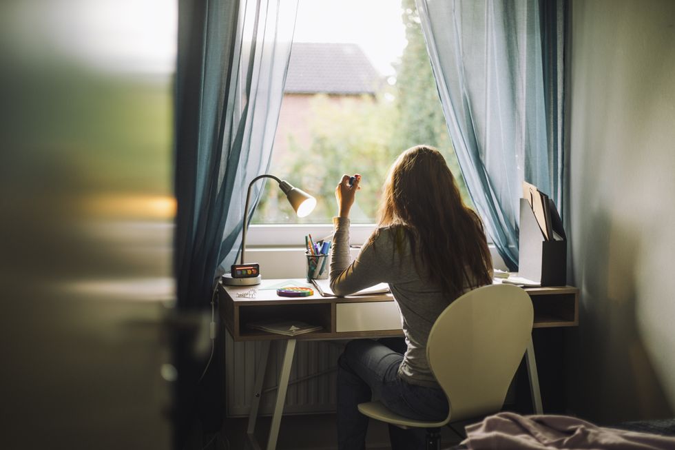 Rear view of teenage girl doing homework while sitting at desk in home