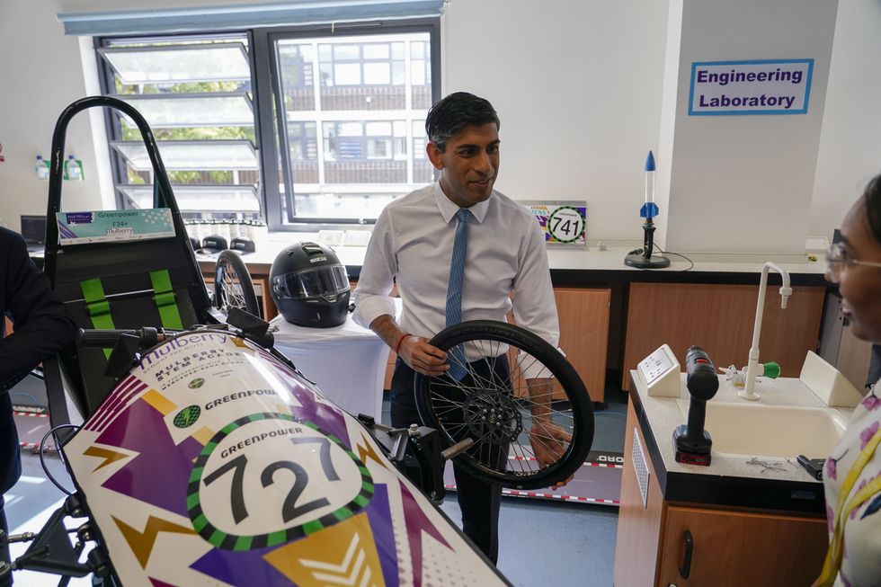 Rishi Sunak holding a wheel next to a car.