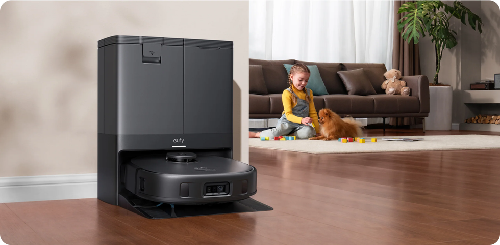 Robot vacuum cleaner docked into the charger. Child playing with dog in the background