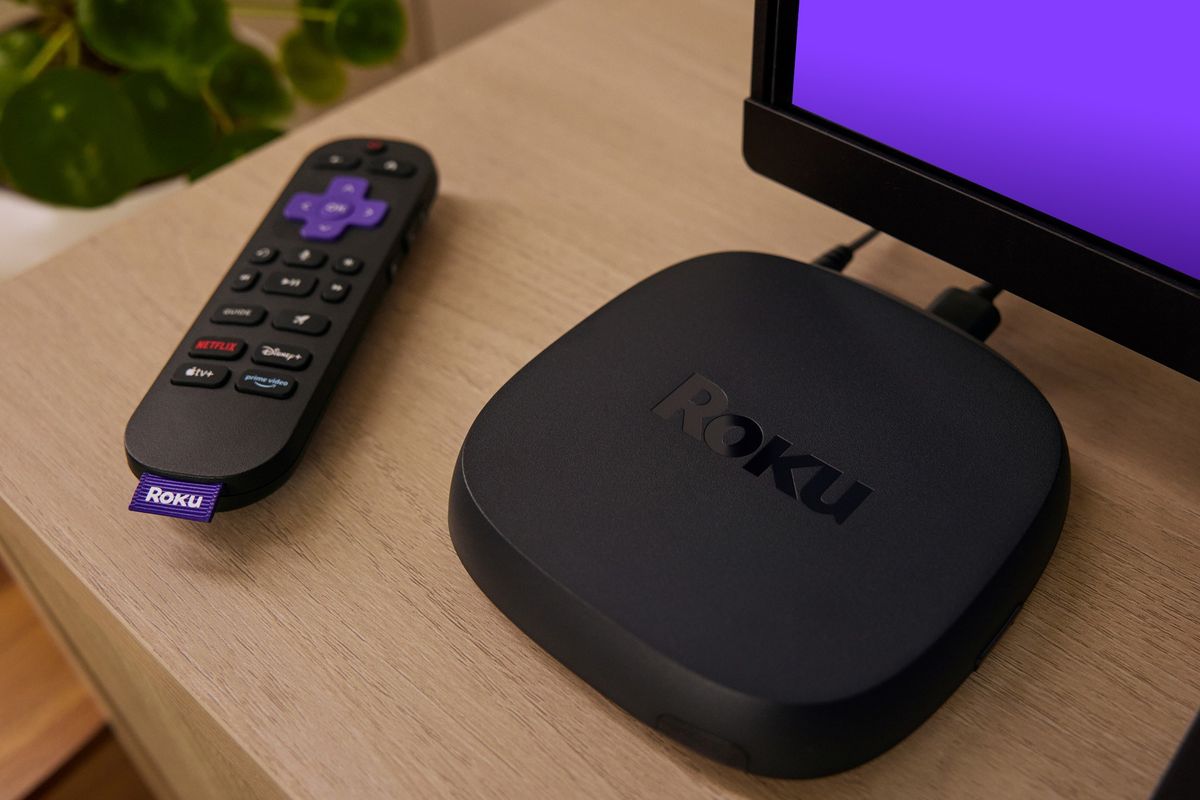 roku remote control on a wooden side with the ultra set-top box pictured next to it with a purple hue coming from the television