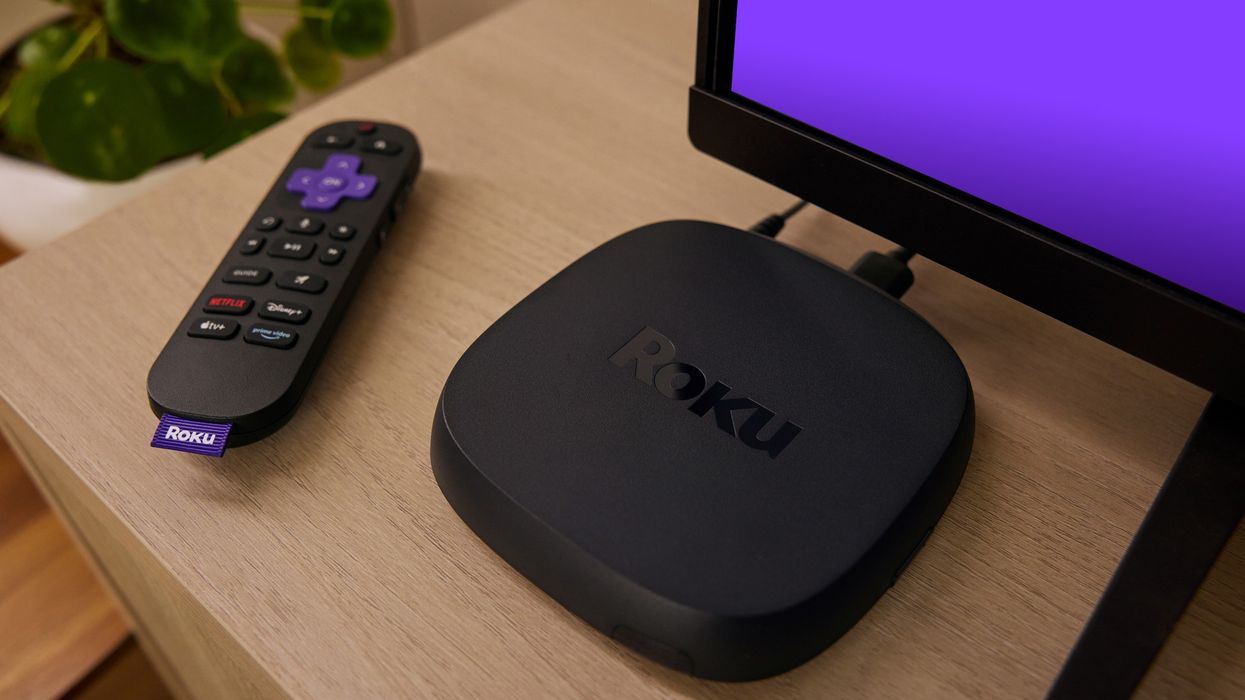 roku remote control on a wooden side with the ultra set-top box pictured next to it with a purple hue coming from the television