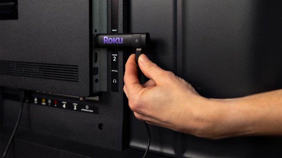 Roku Streaming Stick pictured being plugged into the back of a Smart TV