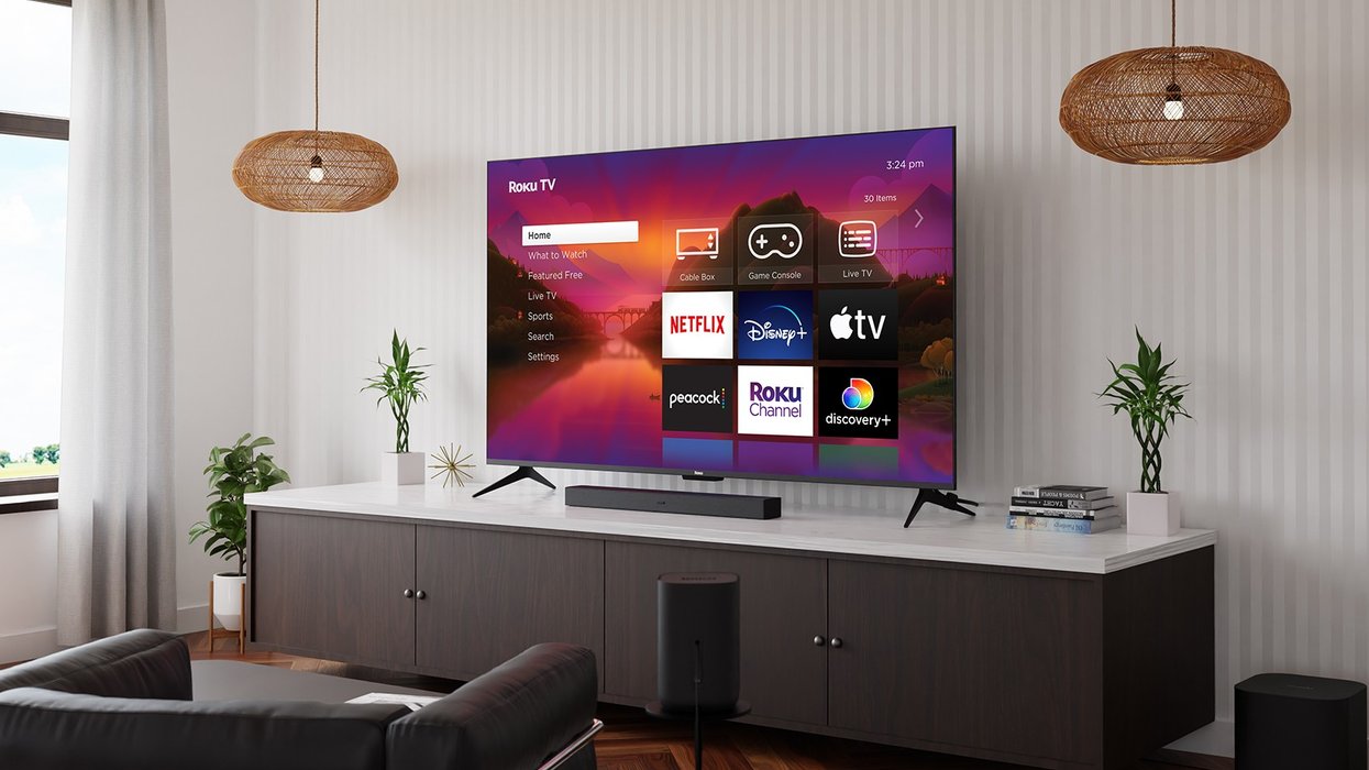 roku tv pictured mounted on the wall of a living room with a selection of streaming services pictured on-screen