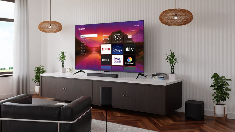 roku tv pictured mounted on the wall of a living room with a selection of streaming services pictured on-screen