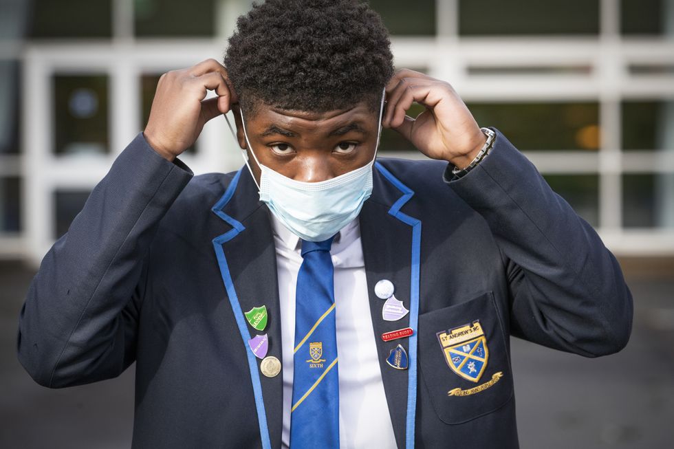 School boy puts on his protective face mask before heading inside for lessons